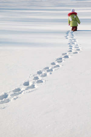 little girl in green jacket walking on snow, footprints in snow, behindの写真素材