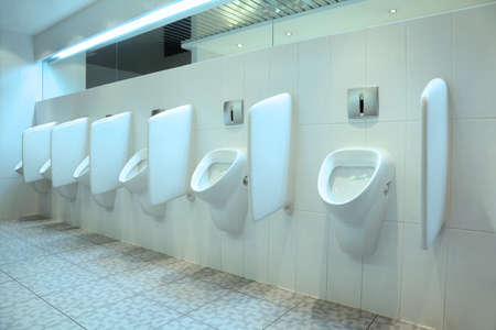 line of six white porcelain urinals in clean, light public toiletsの写真素材