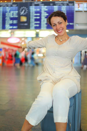 beautiful young woman sitting on their luggage in hall of airport and stretching armsの写真素材