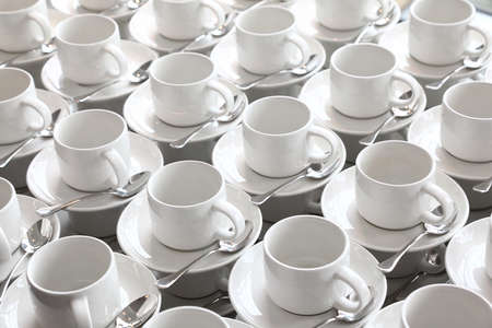 many rows of pure white cup and saucer with teaspoon, reflection on table