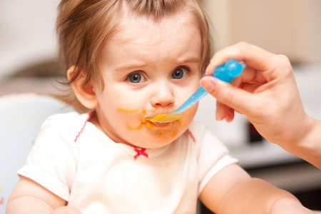 little girl feeding from a spoon on blue chairの写真素材