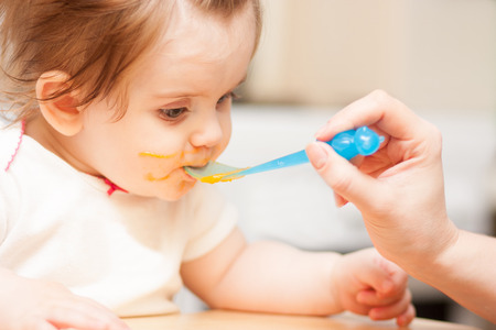 little girl feeding from a spoon on blue chairの写真素材