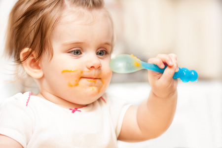 little girl feeding from a spoon on blue chairの写真素材
