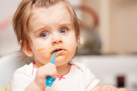little girl feeding from a spoon on blue chairの写真素材