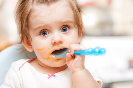 little girl feeding from a spoon on blue chairの写真素材