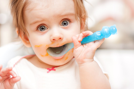 little girl feeding from a spoon on blue chairの写真素材