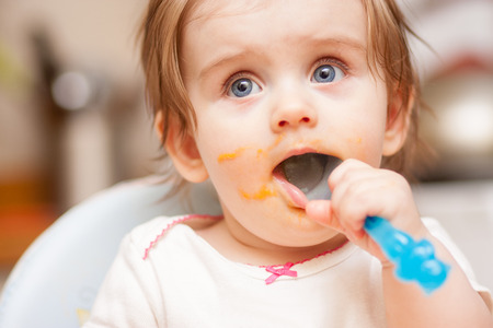 little girl feeding from a spoon on blue chairの写真素材