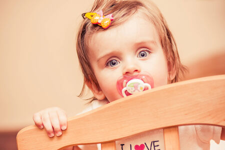 little girl sitting in a crib with a pacifierの写真素材