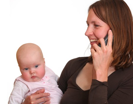 Mother talks to someone over the phone while holding her babyの写真素材