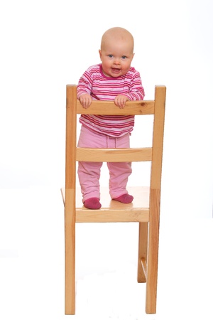 Happy baby girl standing on a chair isolated on white backgroundの写真素材
