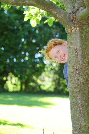 Happy young girl hides behind a tree in the gardenの写真素材