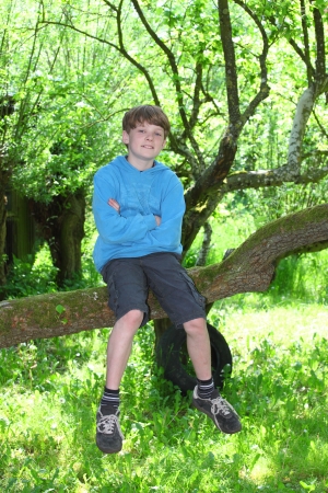 Happy young boy sitting on a branch of a treeの写真素材