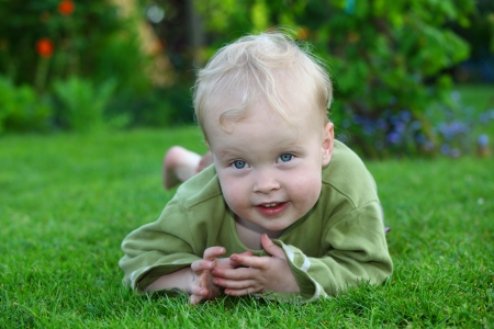 Smiling young toddler lying on grass in the gardenの写真素材