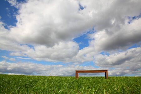 Empty bench on the field with clouds in the skyの写真素材