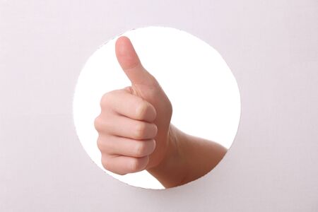 Arm reaches trough a hole with thumbs upの写真素材