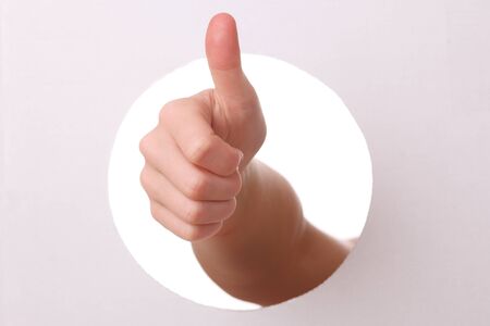 Arm reaches trough a hole with thumbs upの写真素材