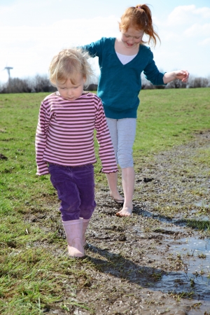 Two kids walking trough a muddy puddleの写真素材