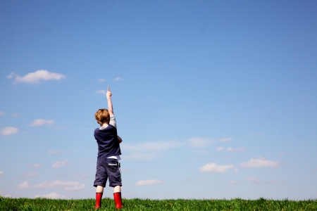 Boy in a meadow pointing to the skyの写真素材