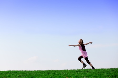 Young girl running on a green meadow with blue skyの写真素材