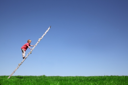 Young boy climbs a ladder on green meadow with blue skyの写真素材