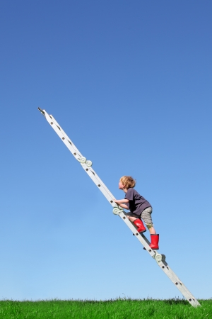 Young boy climbs a ladder on green meadow with blue skyの写真素材
