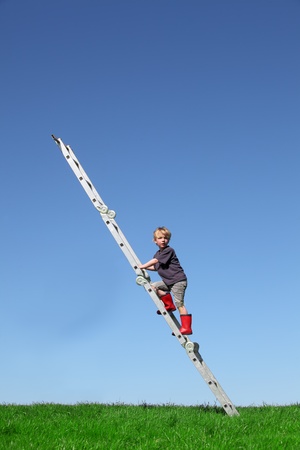 Young boy climbs a ladder on green meadow with blue skyの写真素材
