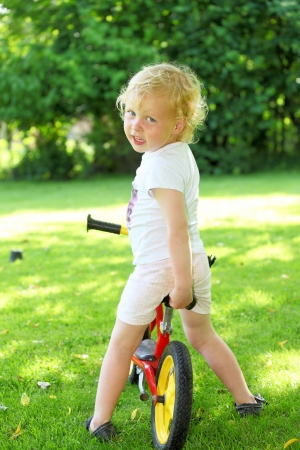Happy young girl on a training bike in the gardenの写真素材