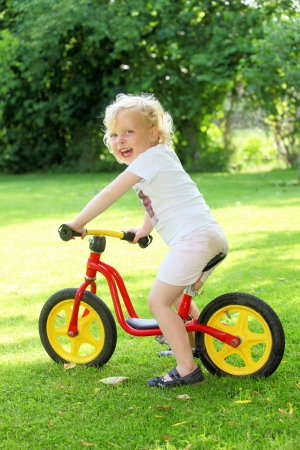 Happy young girl on a training bike in the gardenの写真素材