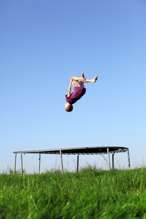 Young boy doing a backflip on a trampoline on green meadowの写真素材