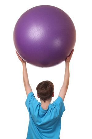 Young boy holding big pilates ball on his head on white backgroundの写真素材