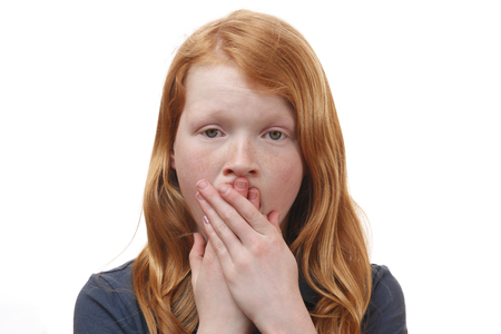 Portrait of a surprised young girl covering her mouth with handsの写真素材