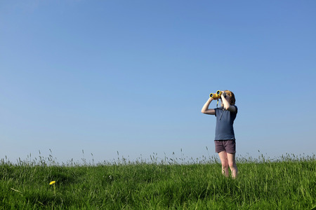 Young girl with binoculars in a meadow searching the skyの写真素材