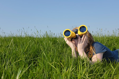 Young girl with binoculars in a meadow searching the skyの写真素材