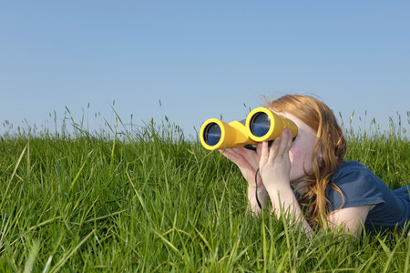Young girl with binoculars in a meadow searching the skyの写真素材