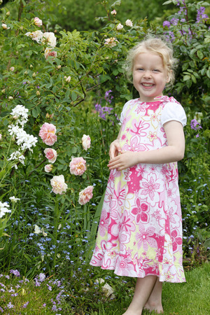 Adorable young girl enjoys some roses in the gardenの写真素材