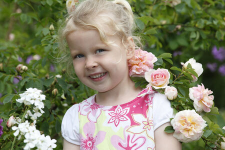 Adorable young girl enjoys some roses in the gardenの写真素材