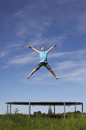 Young boy jumping on a trampoline on green meadowの写真素材