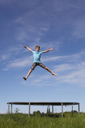Young boy jumping on a trampoline on green meadowの写真素材