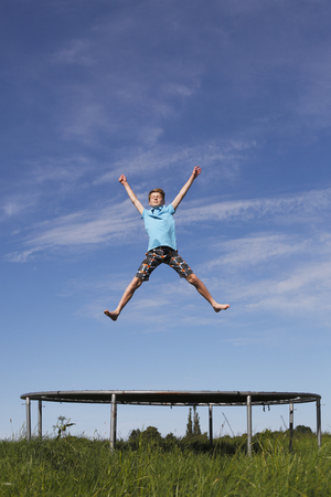 Young boy jumping on a trampoline on green meadowの写真素材