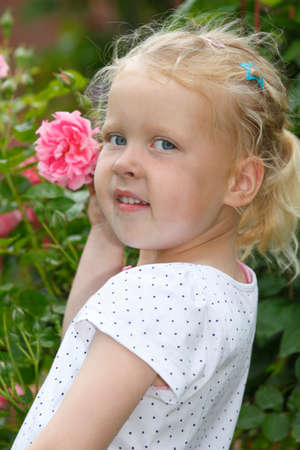 Adorable young girl enjoys some roses in the gardenの写真素材