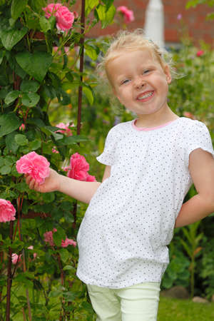 Adorable young girl enjoys some roses in the gardenの写真素材
