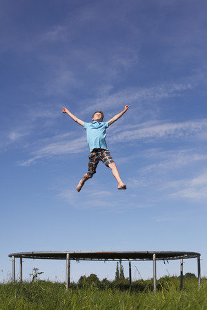 Young boy jumping on a trampoline on green meadowの写真素材