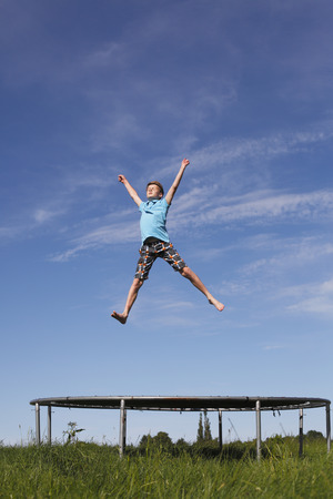 Young boy jumping on a trampoline on green meadowの写真素材
