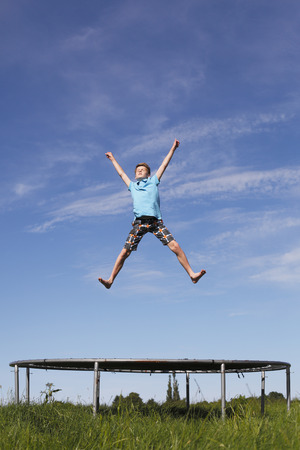 Young boy jumping on a trampoline on green meadowの写真素材