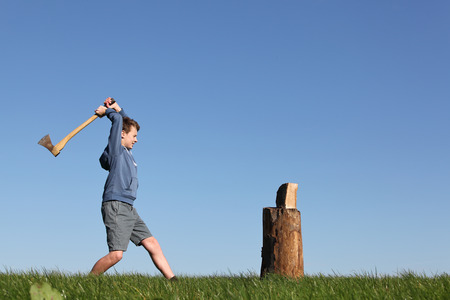 Young boy outdoors chopping wood with blue skyの写真素材