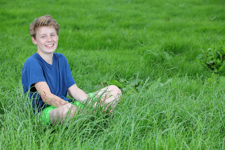 Happy young teenage boy sitting in a meadowの写真素材