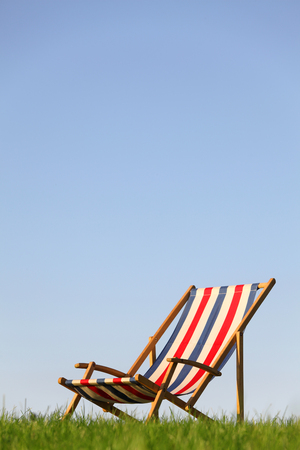 Wooden deckchair in a meadow with blue skyの写真素材