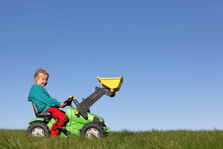 Happy young girl plays on a toy tractor outdoors in the gardenの写真素材