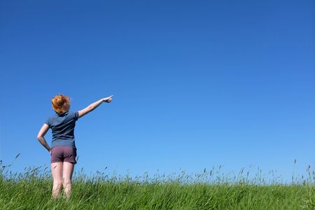 Young girl standing in meadow pointing to skyの写真素材