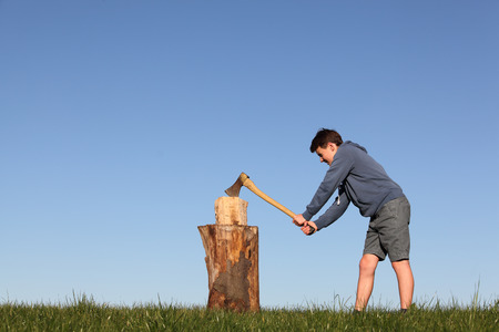 Young boy outdoors chopping wood with blue skyの写真素材